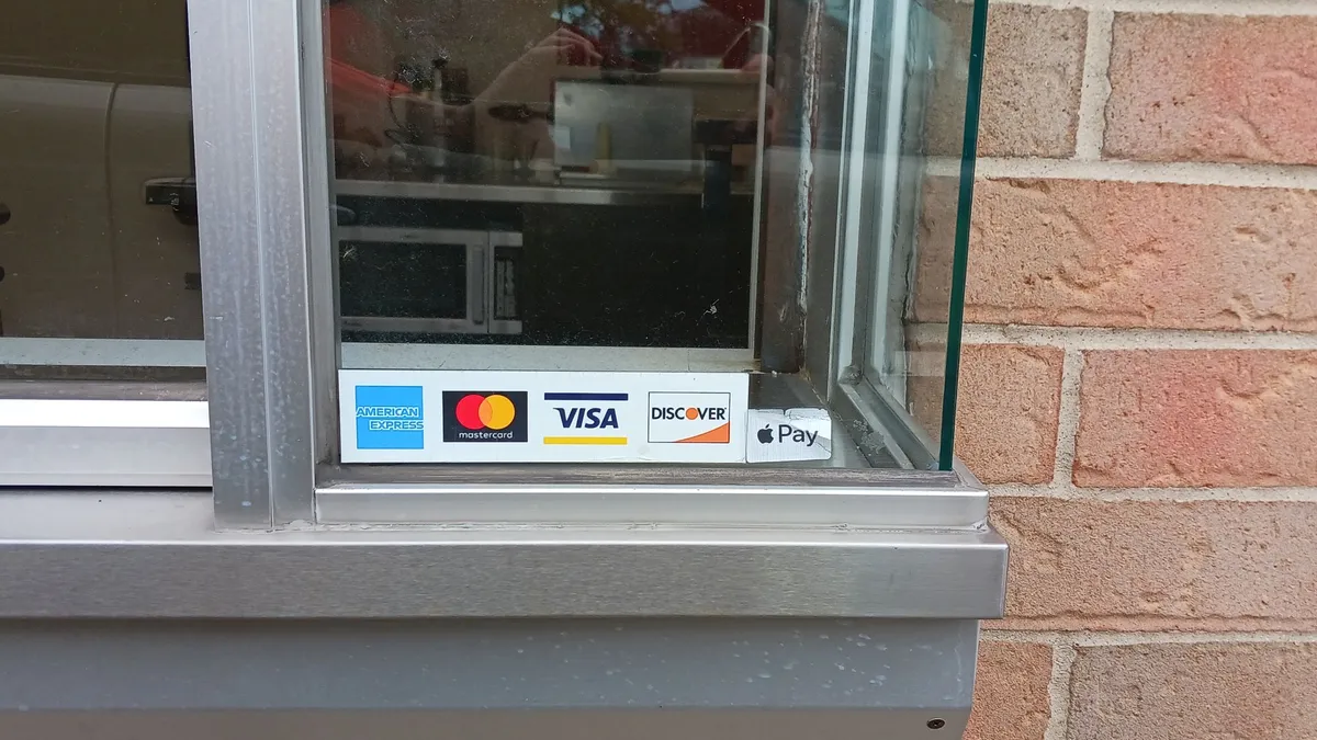 Credit card and payment type logos Visa, Mastercard, Discover and American Express displayed on drive-up window.