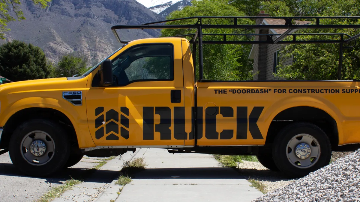 An orange truck with the word "Ruck" on it amid a green, forest backdrop.