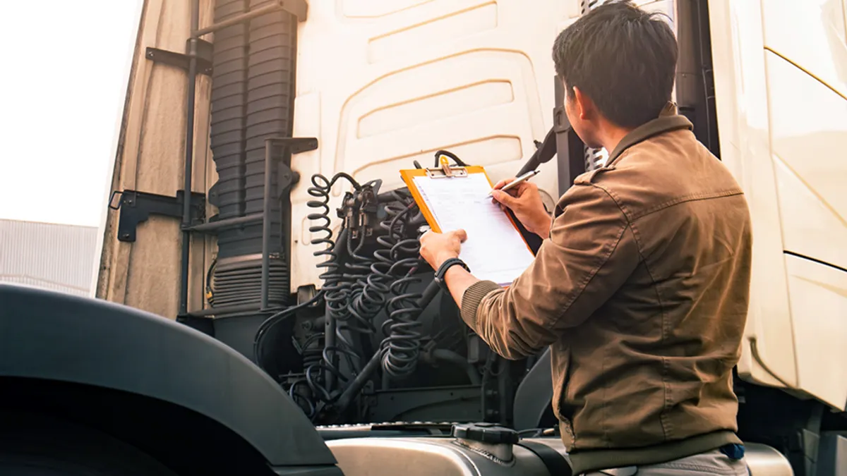 Person holding a clipboard, piece of paper and a pen while looking at the back of a truck.