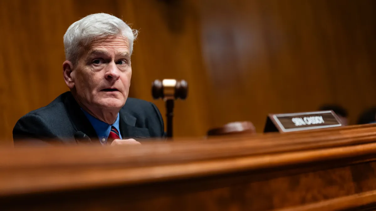 A person holds a gavel while sitting in front of a blurred out sign that says "Sen. Cassidy."