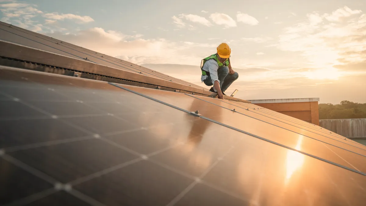 As part of a maintenance check, a service engineer inspects the solar cell on a building roof for a damaged part.