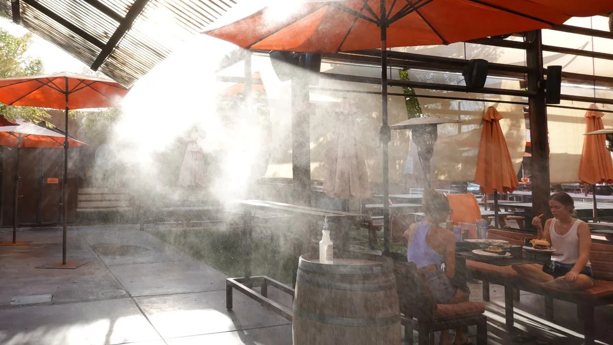 An image of outdoor dining with misters coming off of red umbrellas.