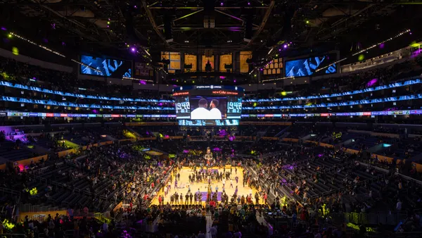 An elevated view of a basketball arena as players and fans file in.