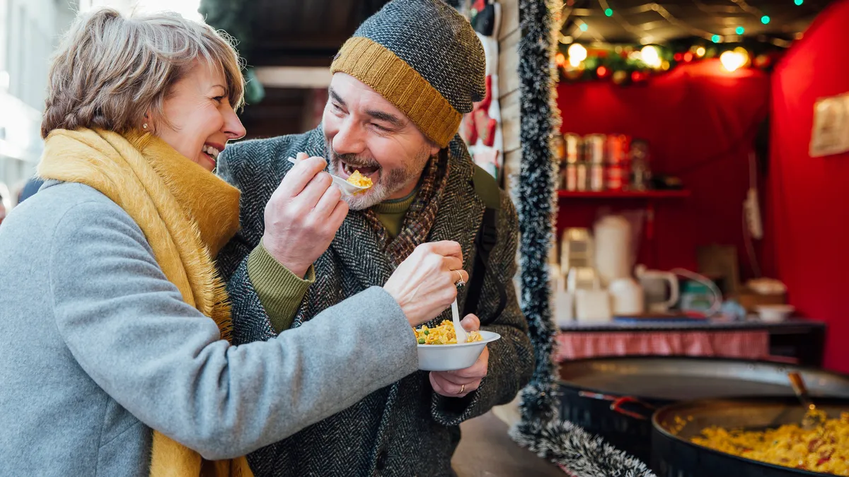 Mature couple are enjoying sharing some paella from a christmas market stall