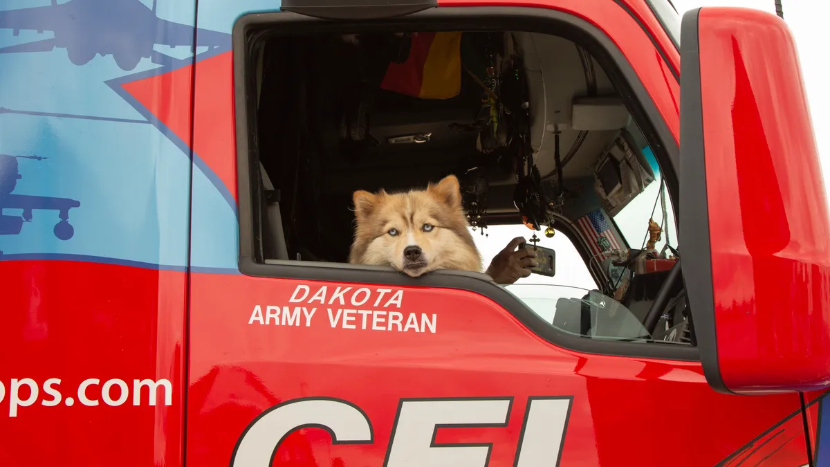 A dog pokes its head through a tractor's window.