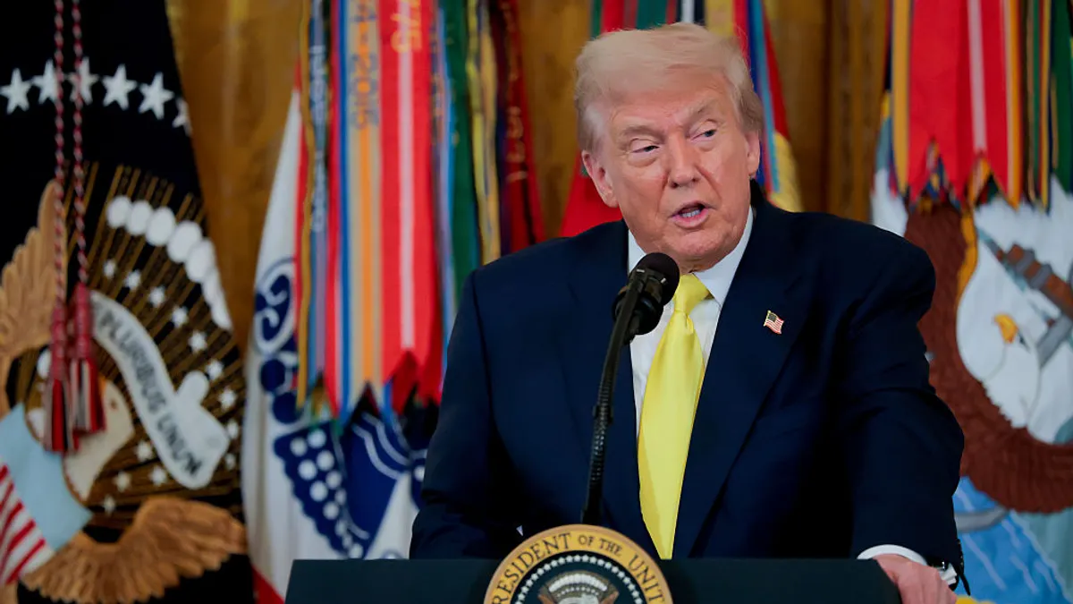 Trump speaks at a podium against a backdrop of flags.