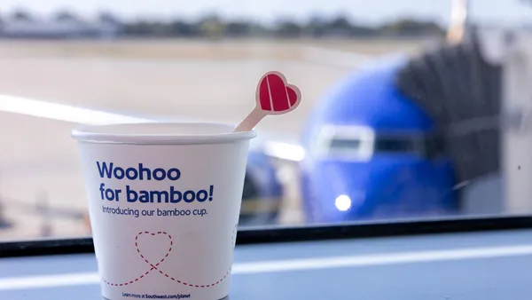 A paper-based cup and a wooden stir stick with Southwest Airlines branding sit on an airline tray table next to a window.