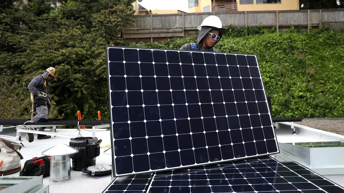 People install a solar panel on a roof.