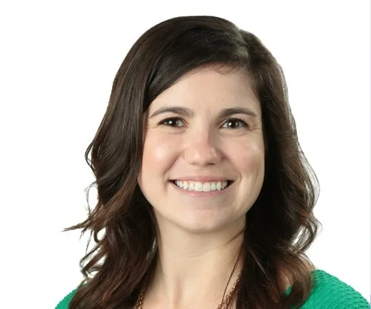 Headshot of a smiling woman with brown wavy hair.