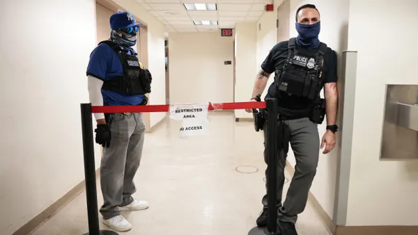 Two people wearing masks and black shirts that say "POLICE" in a hallway
