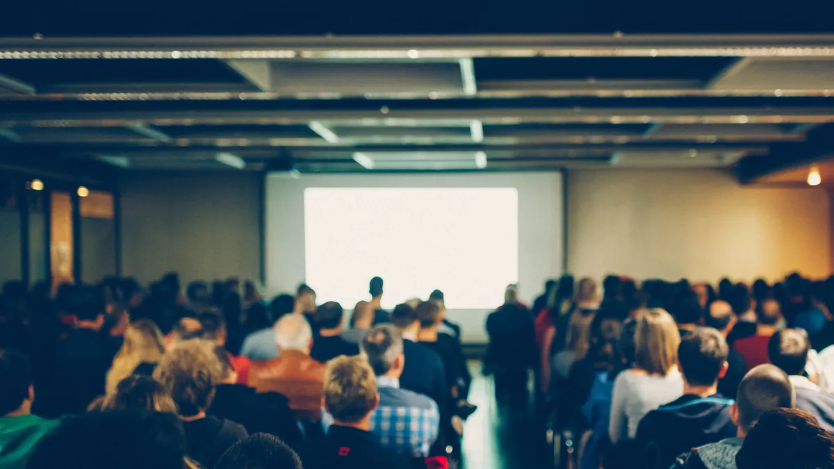 A group of people sit in a conference room in front of a blank screen.