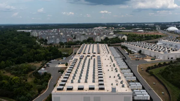 An aerial view of a large gray building amid trees that takes up most of the frame. It is level, and low to the ground.
