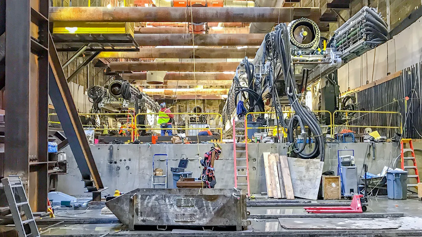 A view of heavy machinery with many overhead pipes in a underground construction site.