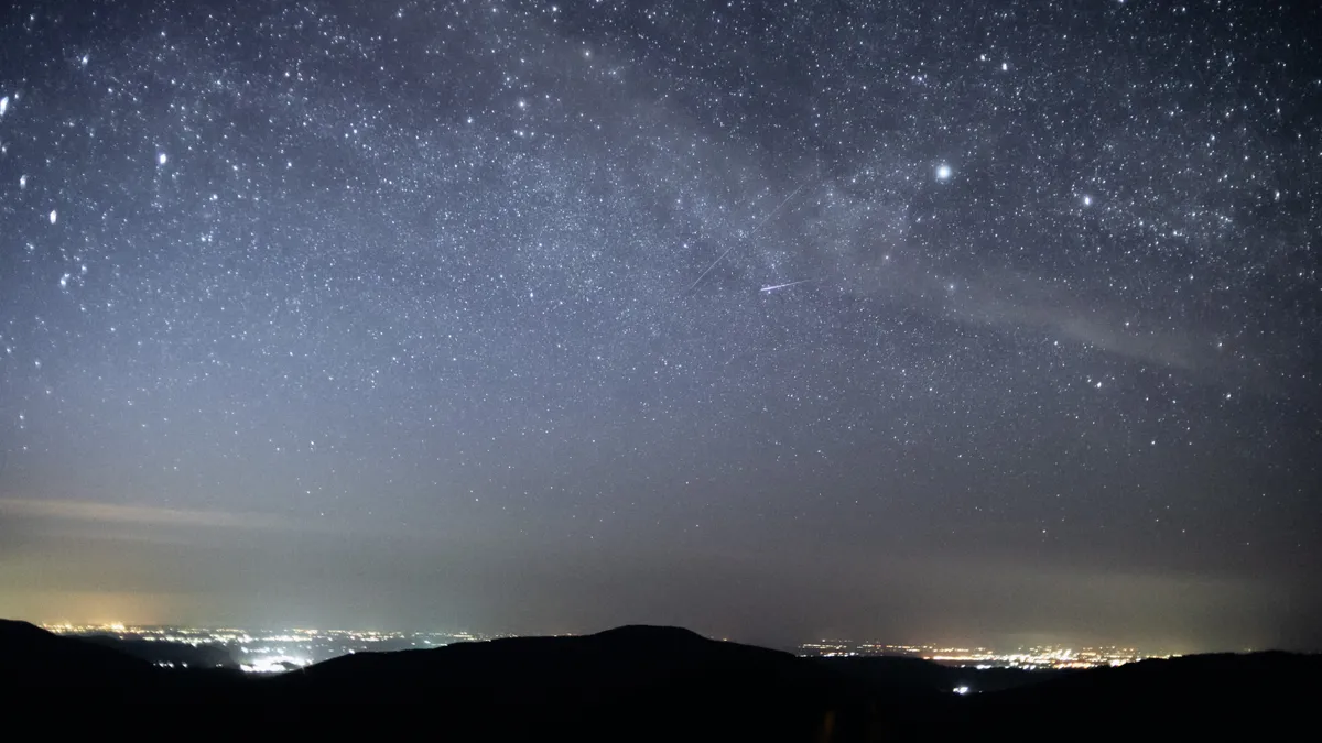 Silhouette of hills and light emanating from faraway buildings under starry night sky