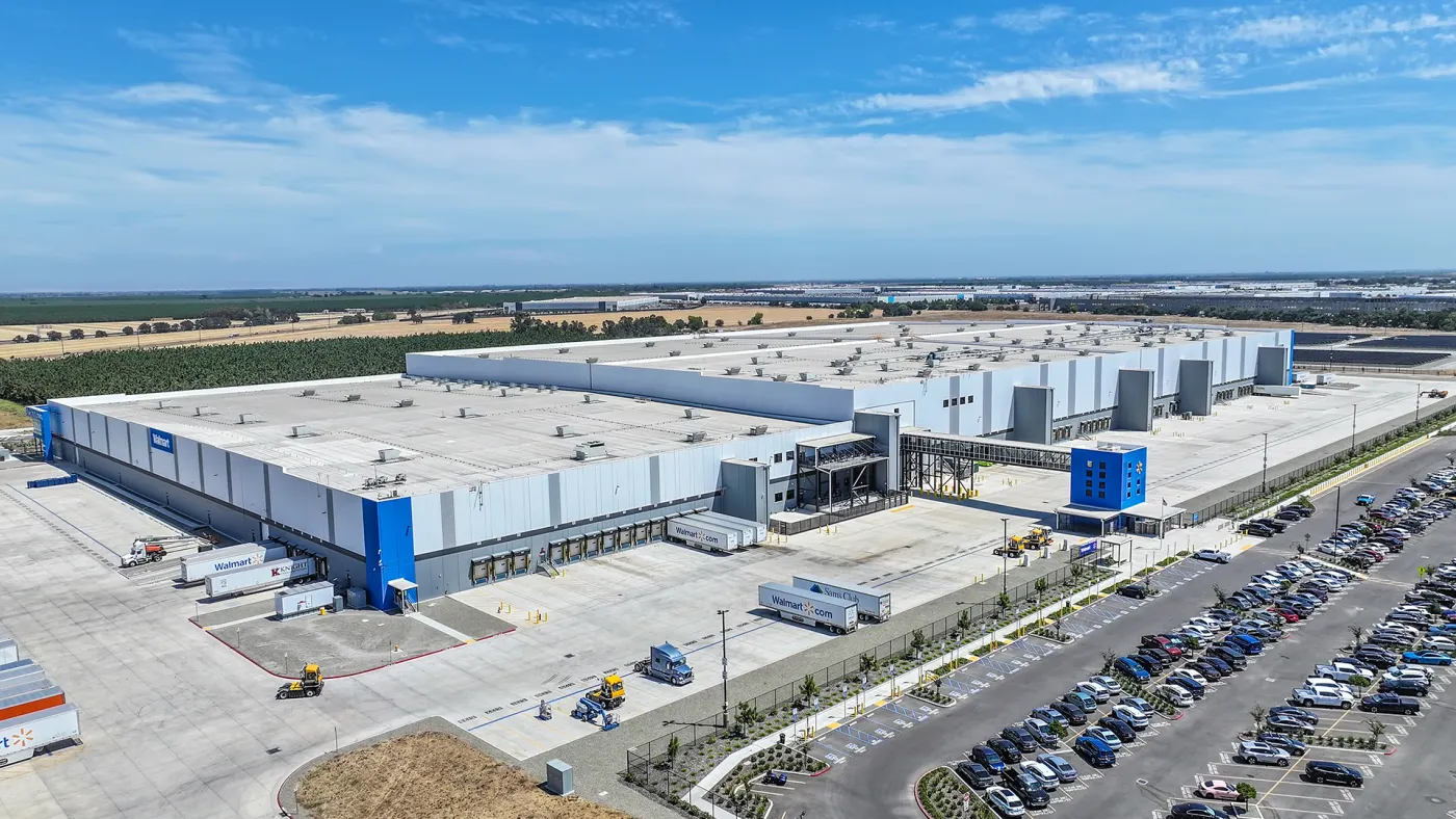 A large warehouse sits on a lot with trucks and a parking lot