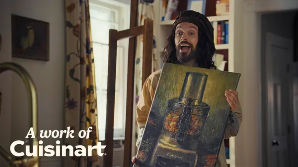 A Baroque period-styled artist holds up an oil painting of a Cuisinart product in a modern kitchen