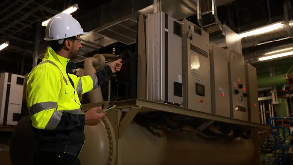 A senior specialist engineer, wearing a green safety jacket, holds a digital tablet during preventive maintenance for industrial HVAC machinery.