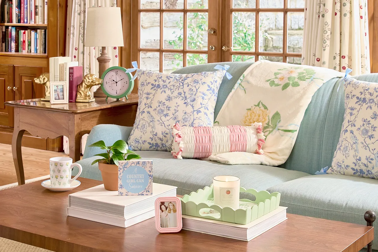 A living room featuring a light blue couch with floral throw blankets and pillows on it from Dollar General's home collection with Holly Williams.