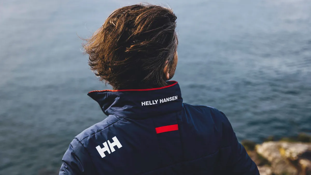 A person wearing a Helly Hansen-branded wind breaker over looks a sea.