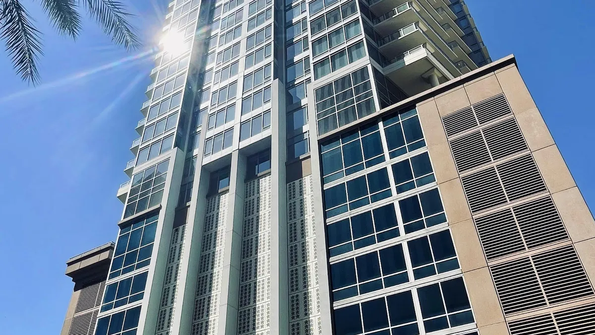 A tower stands upright on a bright, sunny day. The tower is a modern building, covered by windows.