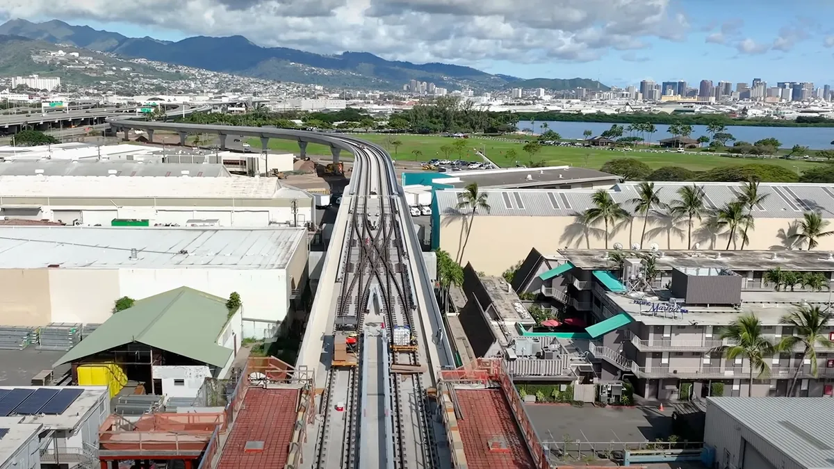 Aerial view of two train tracks running from the foreground to the background, which has mountains and city skyline.