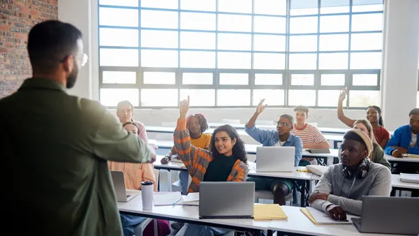 Smiling students asking their teacher questions during a college class