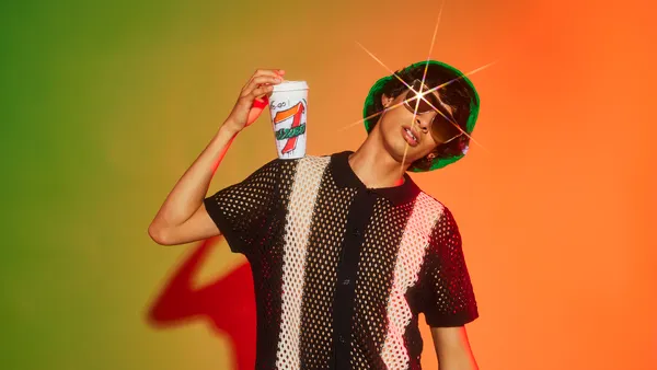 A photo of a person in sunglasses, holding a cup in one hand and looking at the viewer. The cup says 7-Eleven.