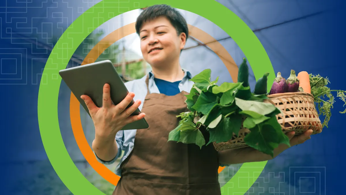 Man in apron holding basket of vegetables and iPad.
