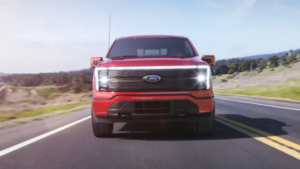 The front view of a red, 2022 Ford Lightning pickup driving on a road.