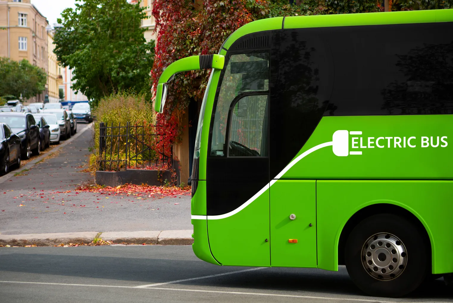 The left front of a green bus on a street is marked as "Electric Bus."