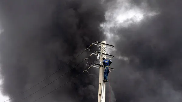 An engineer repairs an electricity pole as smoke billows after overnight airstrikes on oil depots on March 8, 2026 in Tehran, Iran.