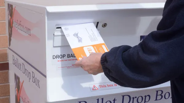 A person inserts an early election ballot envelope into a ballot drop box in Jefferson County, Colorado.
