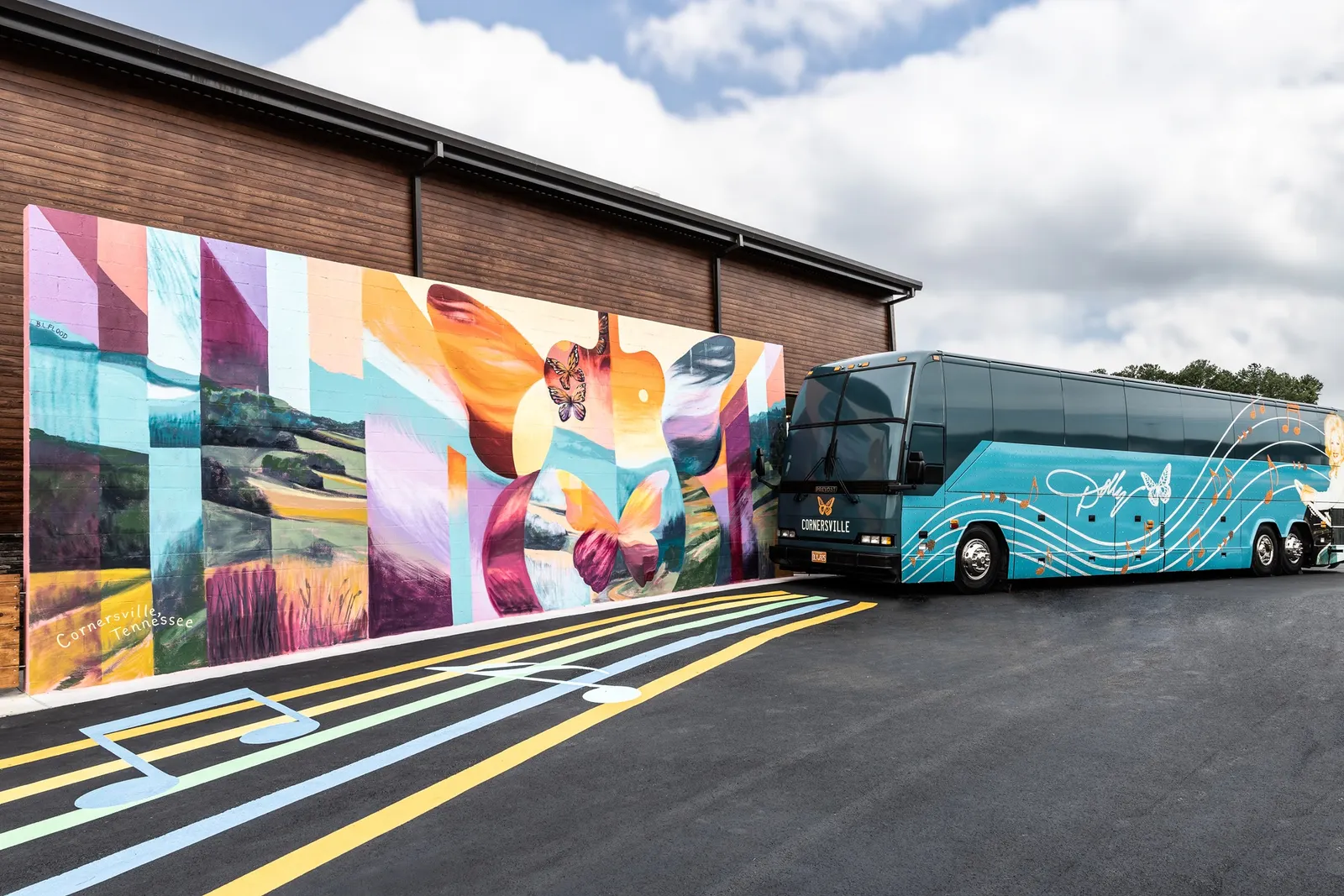 A photo of the exterior of a building. A mural showing Tennessean lanscrapes inside the shapes of a guitar and butterfly is on one wall, next to a tour bus.