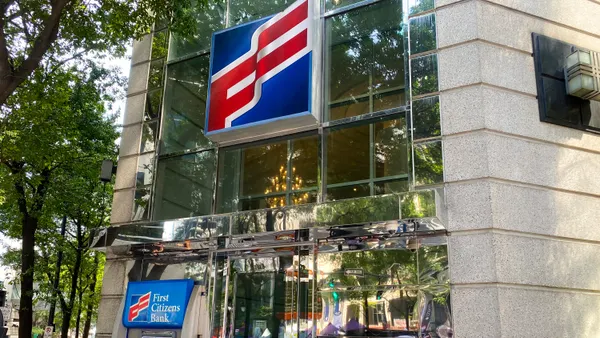 The "First Citizens" logo is shown above a doorway on a stone building with mirror panels. An ATM with the words "First Citizens Bank" sits next to the door.