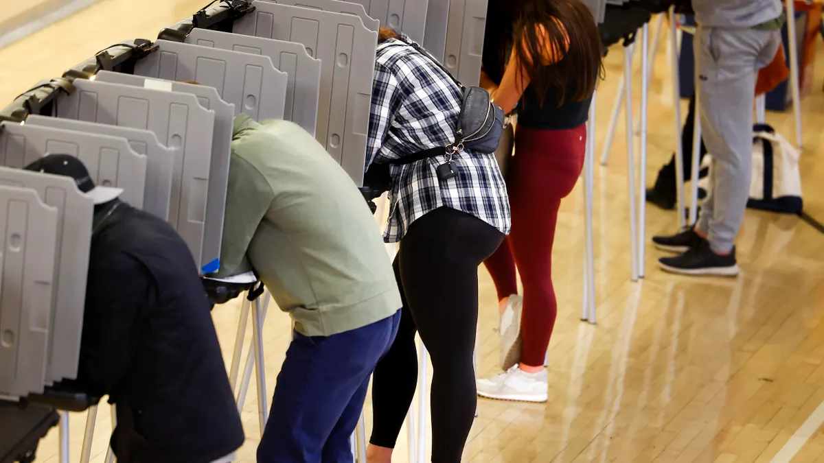 People hunched over a stand with dividers at a voting place.