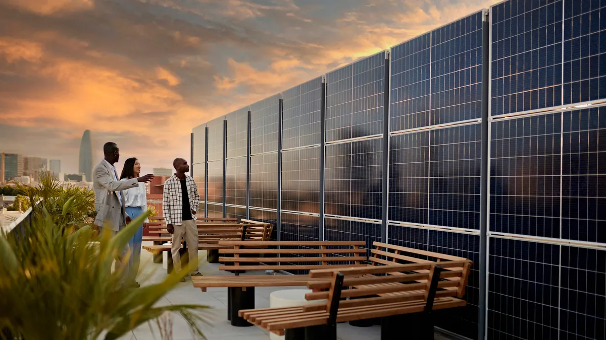 Real estate agent and couple standing on rooftop of environmentally aware office building with dramatic sky and Barcelona cityscape in background at sunset.