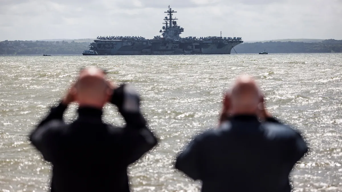 The backs of two men are seen looking through binoculars at the U.S. Navy ship USS George W. Bush.