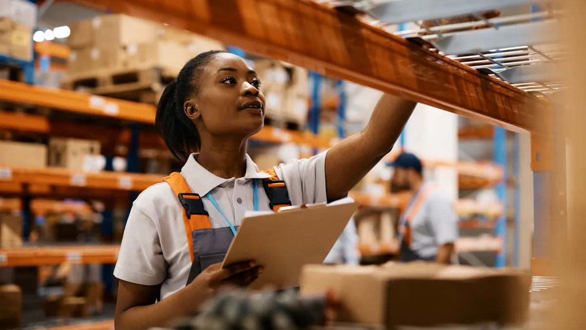 Female worker checking inventory on shelves of distribution warehouse.