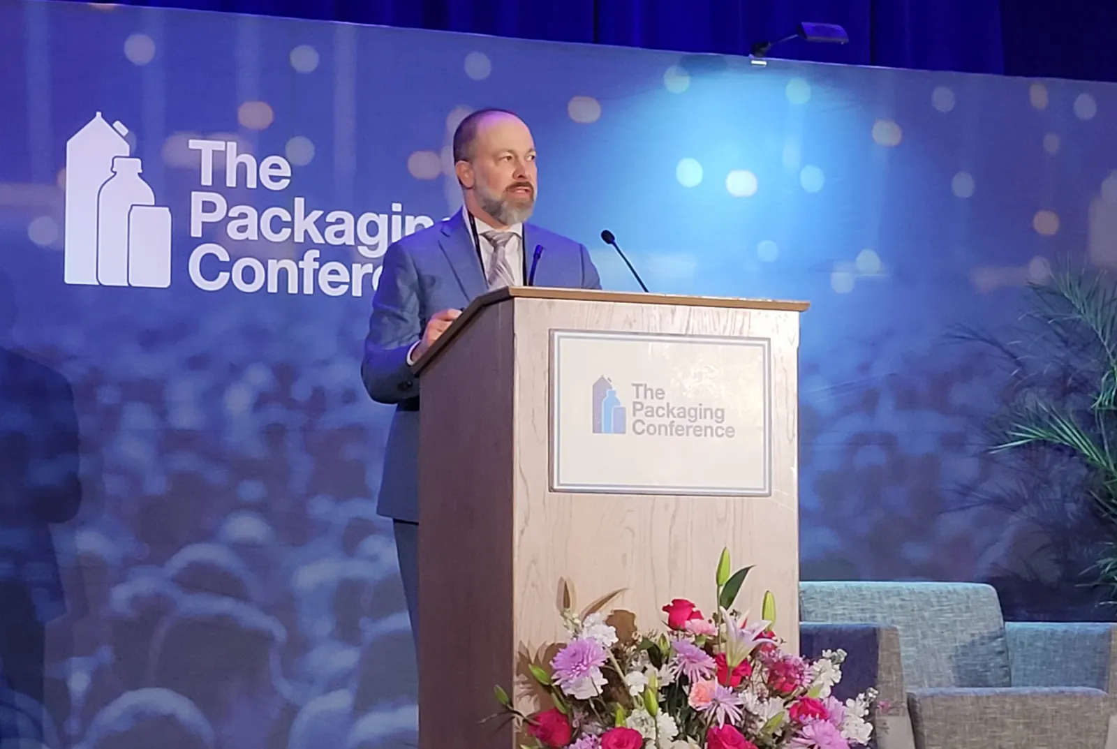 A person stands at a podium that has messaging for The Packaging Conference.