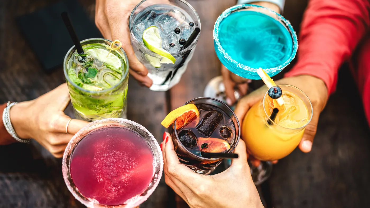 A close up of people holding colorful cocktails