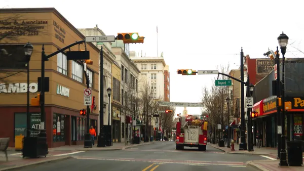 A shot of a town's downtown. A red fire truck is in the foreground on an almost carless downtown street.