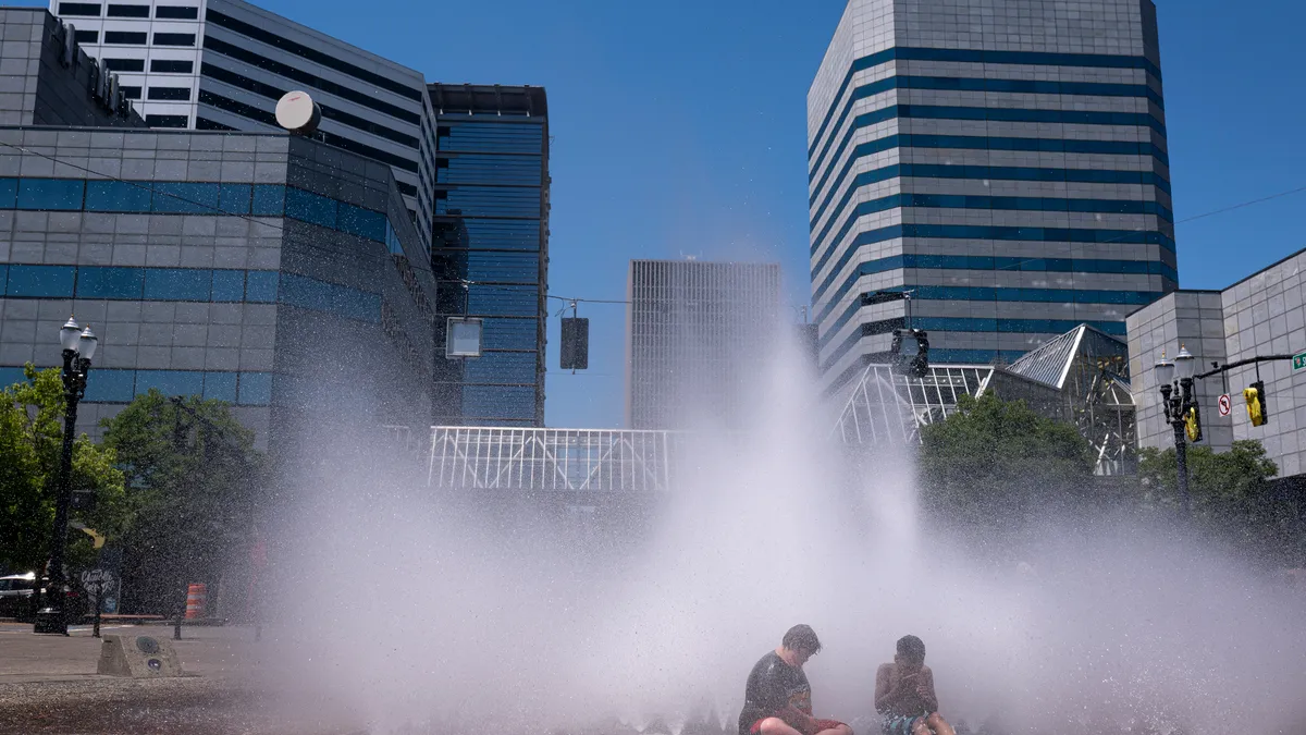 People sit under a fountain in front of buildings