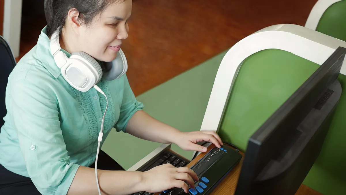 A worker with a visual impairment uses a computer with refreshable braille display and braille terminal.