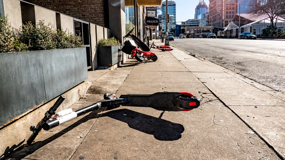 Several scooters lay on their sides along a sidewalk in an urban setting.