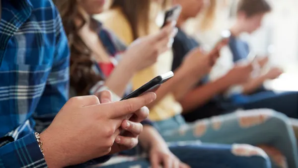 A close-up of mid-sections of people sitting in a row with cellphones in their hands.
