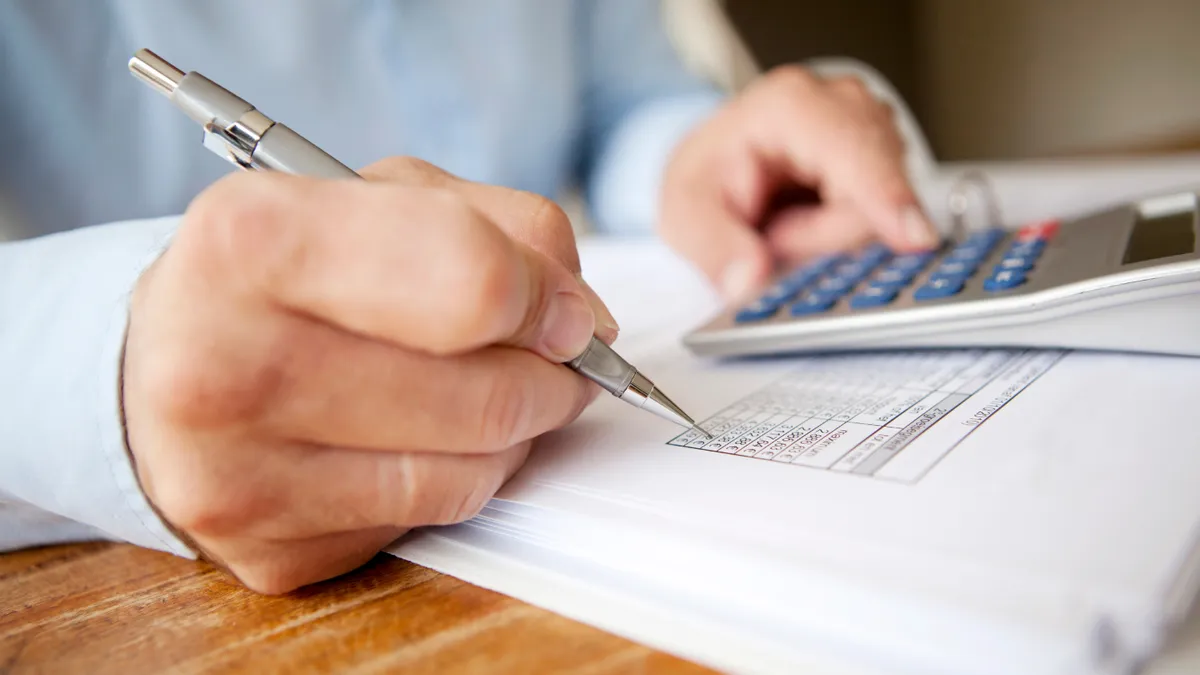 Businessman calculating finances with pen in one hand and calculator in the other.