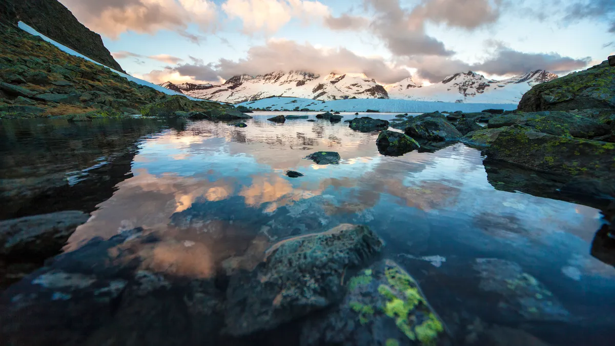 Meditative view from calm alpine lake to mountain vastness. Stones in clear water. stock photo...