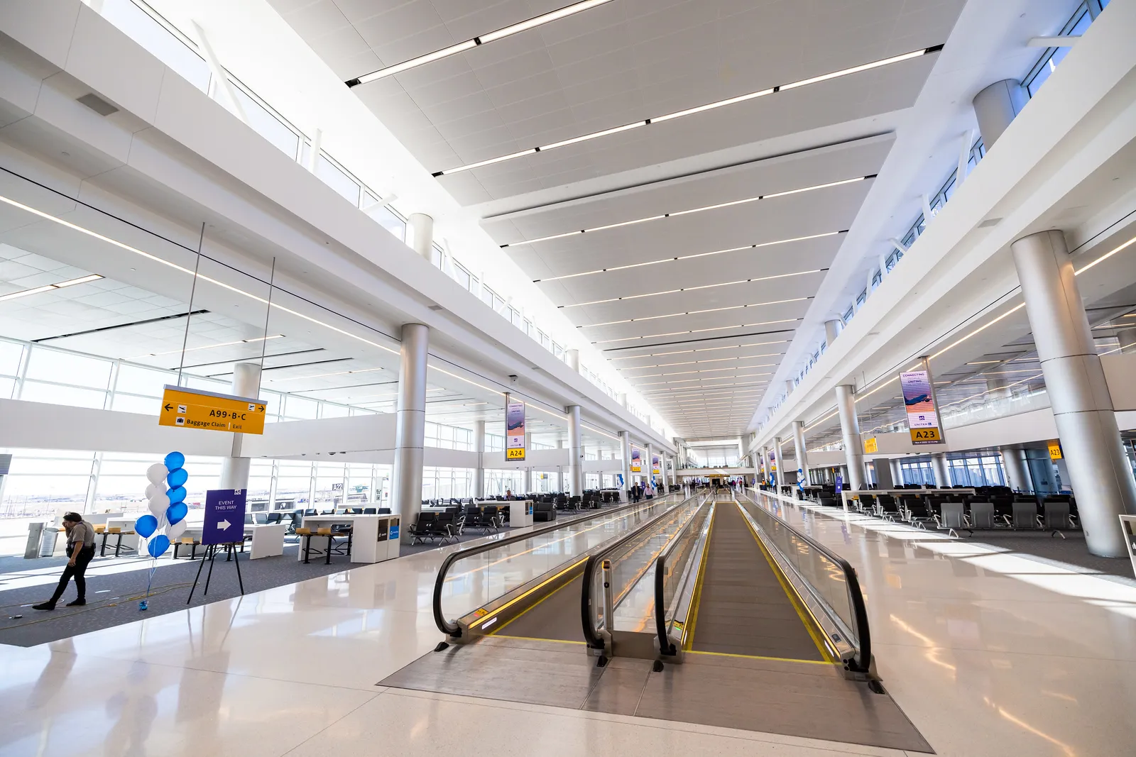 An airy white concourse space with moving sidewalks and seating.