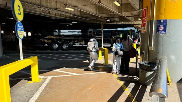 Several people seen from behind walking toward an intercity bus in a garage.