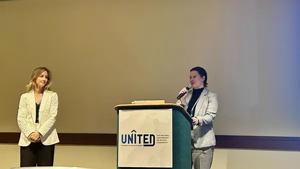 A presenter stands at a podium to the right of another speaker discussing holistic school safety practices.